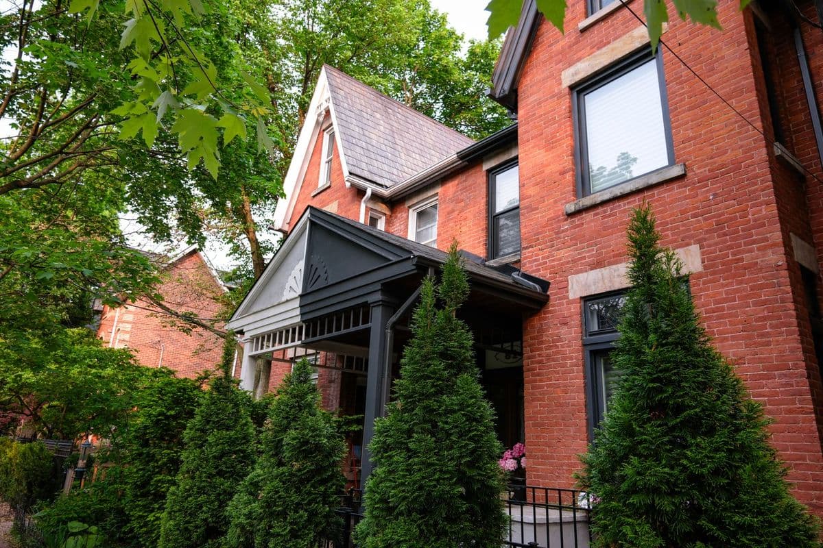 Red brick house with lush greenery in a picturesque Toronto neighborhood.